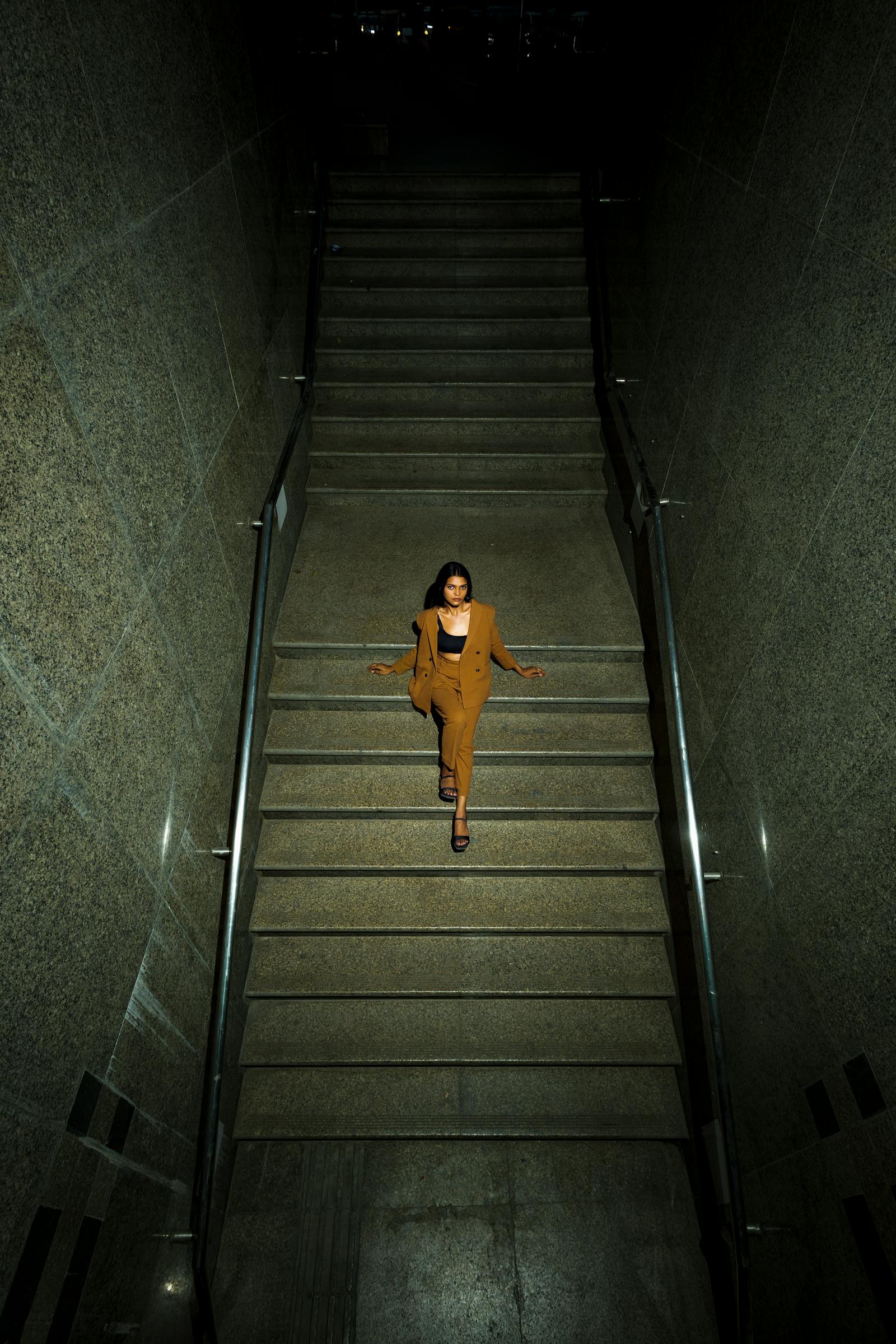 A wide editorial frame — a model in a long camel coat walking through an arched colonnade, late afternoon light cutting across the marble floor.